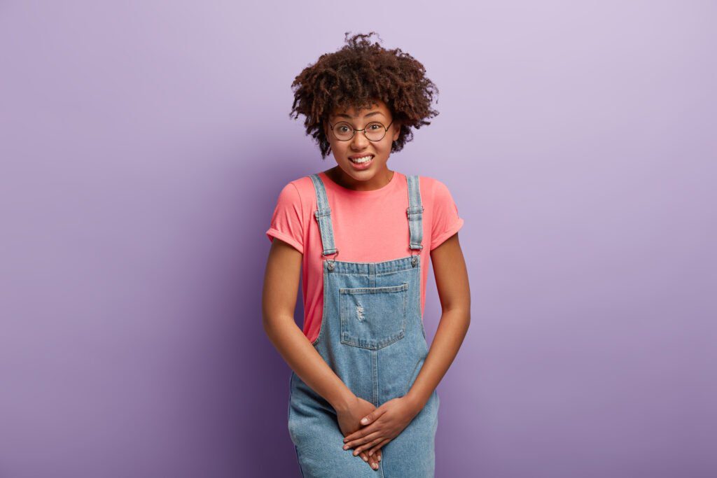 unhappy dark skinned woman holds crotch needs toilet has problematic situation wears pink t shirt denim sarafan suffers from cystitis isolated purple wall people urgency 1024x683 - How to eliminate vaginal odor with just 1 simple natural ingredient.