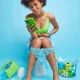 Indoor shot of Afro American woman suffers from abdominal cramps has constipation searches in internet what medicine to take holds mobile phone poses in restroom on toilet bowl. Health problems